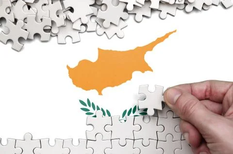 Cyprus flag  is depicted on a table on which the human hand folds a puzzle of Foto stock