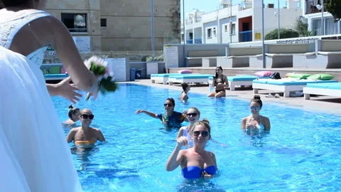 CYPRUS, SENTEMBER 2018: Chic smiling bride throws a bouquet in the pool with her Video stock 96339265