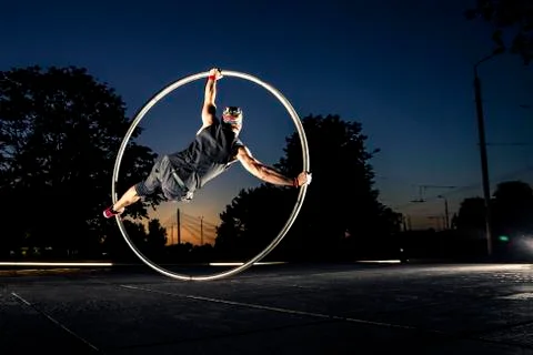 Cyr wheel performance session by young man at night. Stock Photos