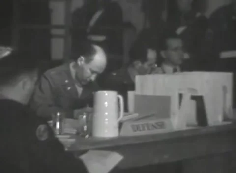 DACHAU, GERMANY - 1947: Counsel table - Officer studies papers by pitcher Stock Footage 344490870