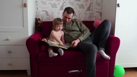 Dad and child are sitting on the couch and looking at pictures in the book Stock Footage 171302000