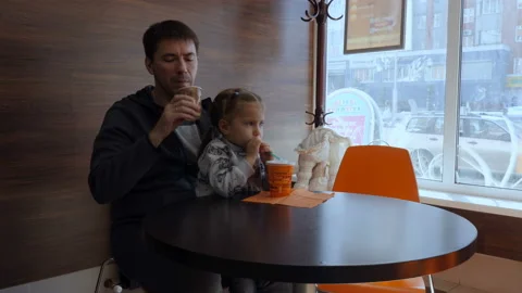 Dad and daughter are drinking coffee, a milkshake at the cafe. 库存影片 88851514