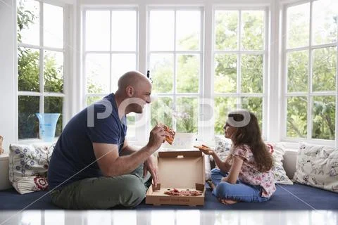 Dad and daughter sit on window seat at home sharing a pizza Stock Photos