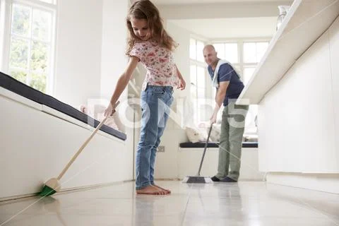 Dad and daughter sweeping the kitchen floor together Stock Photos