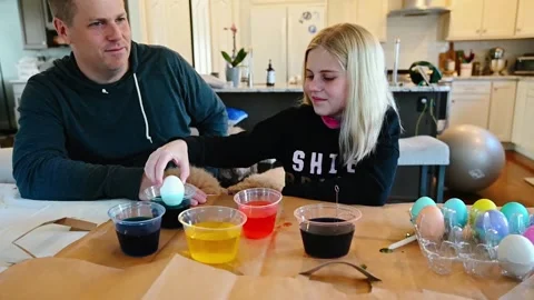 Dad and girl dyeing Easter eggs in kitchen with dog jumping up Video stock 152729532