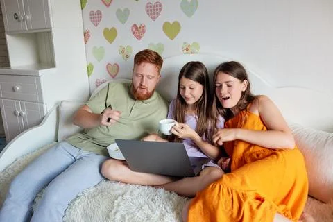 Dad and his daughters on a bed, watching something on a laptop. Girls are e.. Stock Photos