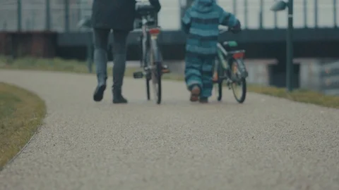 Dad and Kid with bikes walking away from playground Stock Footage 99880481