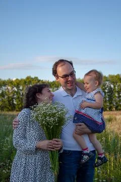 Dad and mom look at their daughter and smile. mom has chamomile in her hands Stock Photos