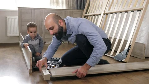 Dad and son are on the floor assembling parts for a new bed in the living Stock Footage 220141269