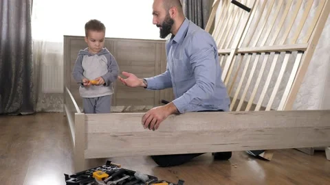 Dad and son are on the floor assembling parts for a new bed in the living Stock Footage 220173792