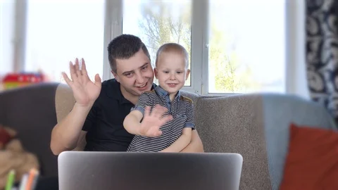 Dad and son are looking at the laptop. Video call with relatives. Dad and son wa Stock Footage 128068771