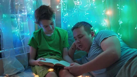 Dad and son are reading a book lying on the couch. into the light of the Stock Footage 170783961