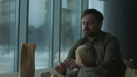 Dad and son eating fast food meal in a cafe, a large window. Video stock 73520346