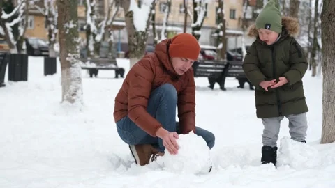 Dad and son make a snow globe for a snowman in a winter park. Stock Footage 167678595