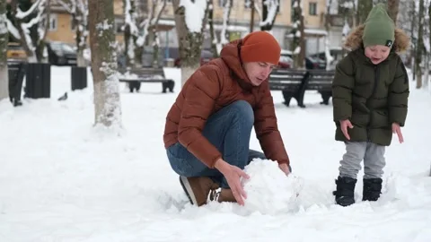 Dad and son make a snow globe for a snowman in a winter park. Stock Footage 167679293