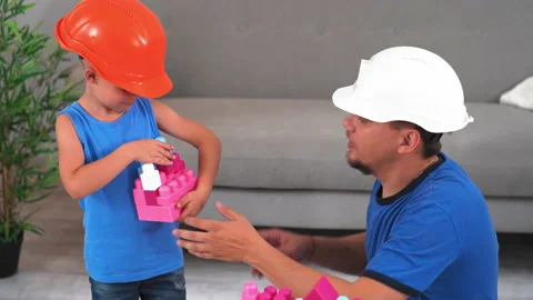 Dad and son making castles wearing construction helmets playing brick Stock Footage 131834755