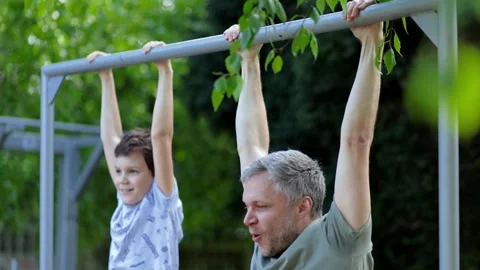 Dad and son pulled up on steel bar outdoors in summer day.play sports and spend  Stock Footage 240924937