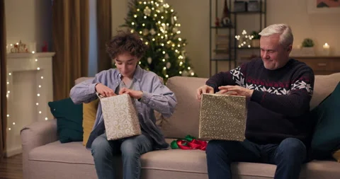 Dad and son sitting on couch in the living room, smiling and holding Christmas 動画素材 210597301