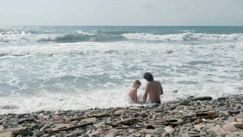 Dad and son is sitting in sea waves in storm on stone beach. Back view. Stock-Footage 116024426