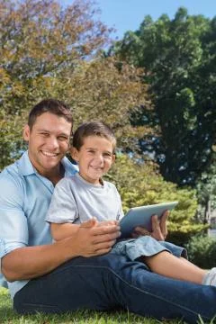 Dad and son with tablet pc smiling into the camera Stock Photos