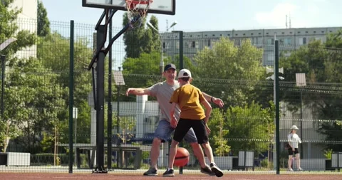 Dad and son train basketball on street court in sunny weather. Father plays Vidéo 329865486