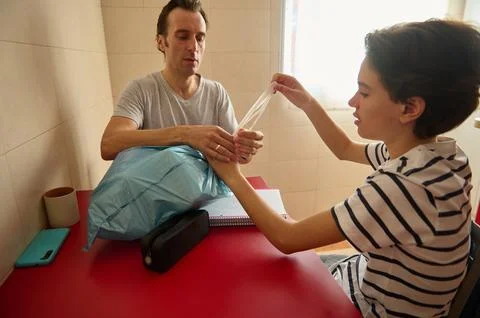 Dad and Son Unpacking Plastic Bag At Red Table During Home Setup Stock Photos