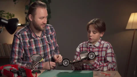 Dad and son using soldering iron for repairing electronic toy car at home Stock Footage 255216709