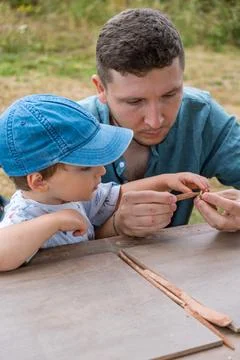 Dad and young son work at the grey table, moulding figures out of red clay Stock Photos