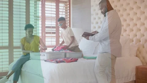 Dad checking tablet checklist starting packing mom folding clothes bed son Stock Footage 333803446