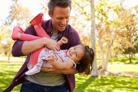 Dad cradling toddler daughter in his arms at the park Stock Photos