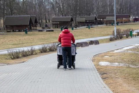 A dad with a double pram strolls through a cold, deserted city park in early  Stock Photos