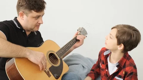 Dad explains to his son how to play guirat slowly front view slow motion Stock Footage 112556770