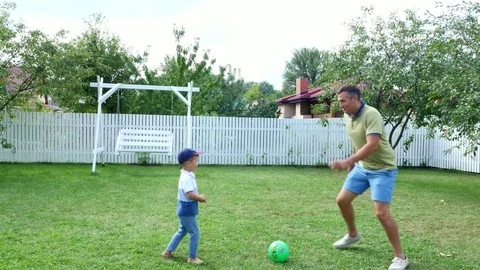 Dad with a four-year-old son playing ball, football, in the yard on a green lawn Stock-Footage 80442292