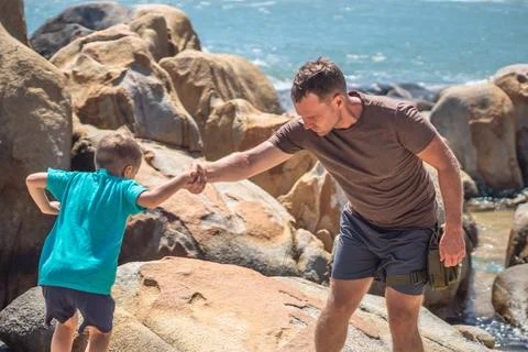 Dad help son jump down over stone, walk spend time together. Man hold kid hand Stock Photos