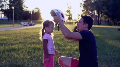 Dad helps his daughter to put on a helmet to safely ride a bike in the city park Stock Footage 78480617