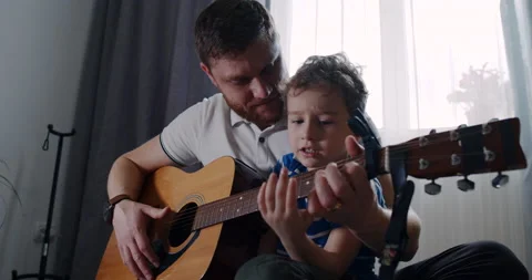 Dad helps his son play the guitar at home Stock Footage 153468256