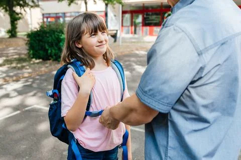 Dad helps to put on a backpack to put on a schoolgirl daughter. The girl smiles Stock Photos