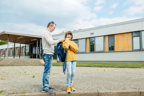 Dad helps to put on a backpack to put on a schoolgirl daughter. The girl smiles Stock Photos