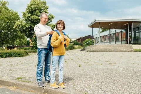 Dad helps to put on a backpack to put on a schoolgirl daughter. The girl smiles Stock Photos