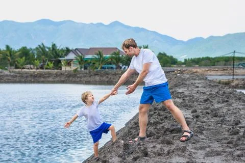 Dad helps son go down to lake water, explains safety rules. Family together walk Stock Photos