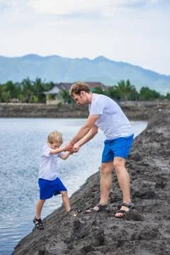 Dad helps son go down to lake water, explains safety rules. Family together walk Stock Photos