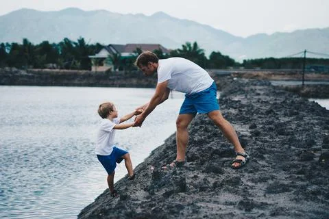 Dad helps son go down to lake water, explains safety rules. Evening, mountain Stock Photos