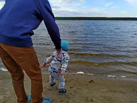 Dad holds his son, while he throws pebbles into the water of the lake Stock Photos
