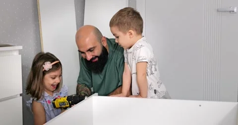 Dad with kids assembling a wardrobe on his own at home in the children's room Stock Footage 276688726
