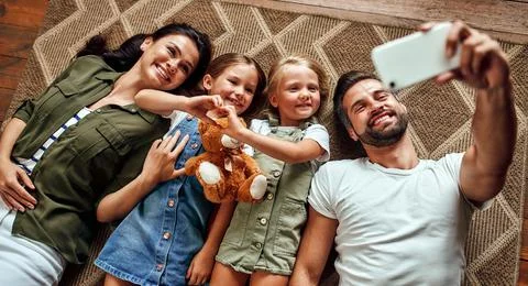 Dad, mom and two cute daughters lie on the carpet on the floor in the living  Stock Photos