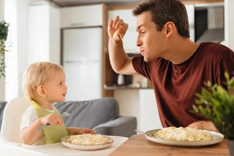 Dad playing with spaghetti while having dinner with his baby boy learning to eat Stock Photos