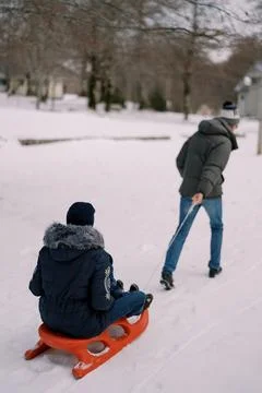 Dad is pulling a sled with mom and a child on a string through the snow. Back 写真素材