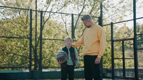 Dad puts his arm around his son while talking at basketball court on a sunny day Stock-Footage 166836247