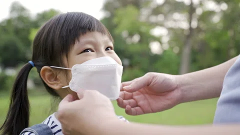 Dad putting on a protective mask on his daughter’s face outdoors in the park. Stock Footage 172295523