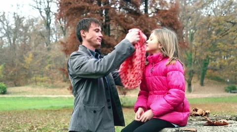 Dad putting red cap on daughter's head and scarf in the park Stock Footage 59553982